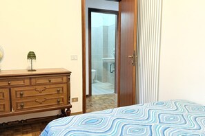 A bedroom with a patterned bedspread, a wooden dresser, and a door leading to a bathroom. - SE154 – Senigallia, large four-room apartment convenient to services (Senigallia)