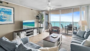 A modern living room with a large TV, comfortable seating, a ceiling fan, and a balcony with a view of the ocean. - Perfect Getaway - Amazing Views Beach Front 2 Beds 2 Baths Hidden Dunes (Miramar Beach)