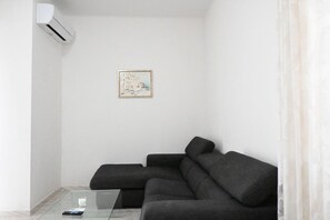 A modern living room with a sectional sofa, a glass coffee table, a framed picture on the wall, and an air conditioning unit. - SE144 – Senigallia, comfortable three-room apartment with air conditioning (Senigallia)