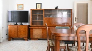 Ein Essbereich mit Holztisch und -stühlen, einem Fernseher auf einem Schrank und einer Vitrine mit verschiedenen Gegenständen.