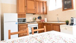 Eine kleine Küche mit Holzausbau, einem weißen Kühlschrank, einer Mikrowelle, einem Herd, einer Spüle und einer Kaffeemaschine.