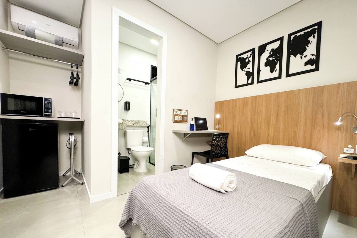 A modern hotel room with a bed, a desk, a microwave, and a refrigerator.