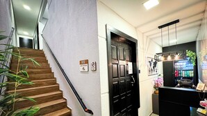 A staircase with a handrail, a black door with a sign, and a reception area with a counter and a refrigerator. - Hotel São José (Sao Jose)