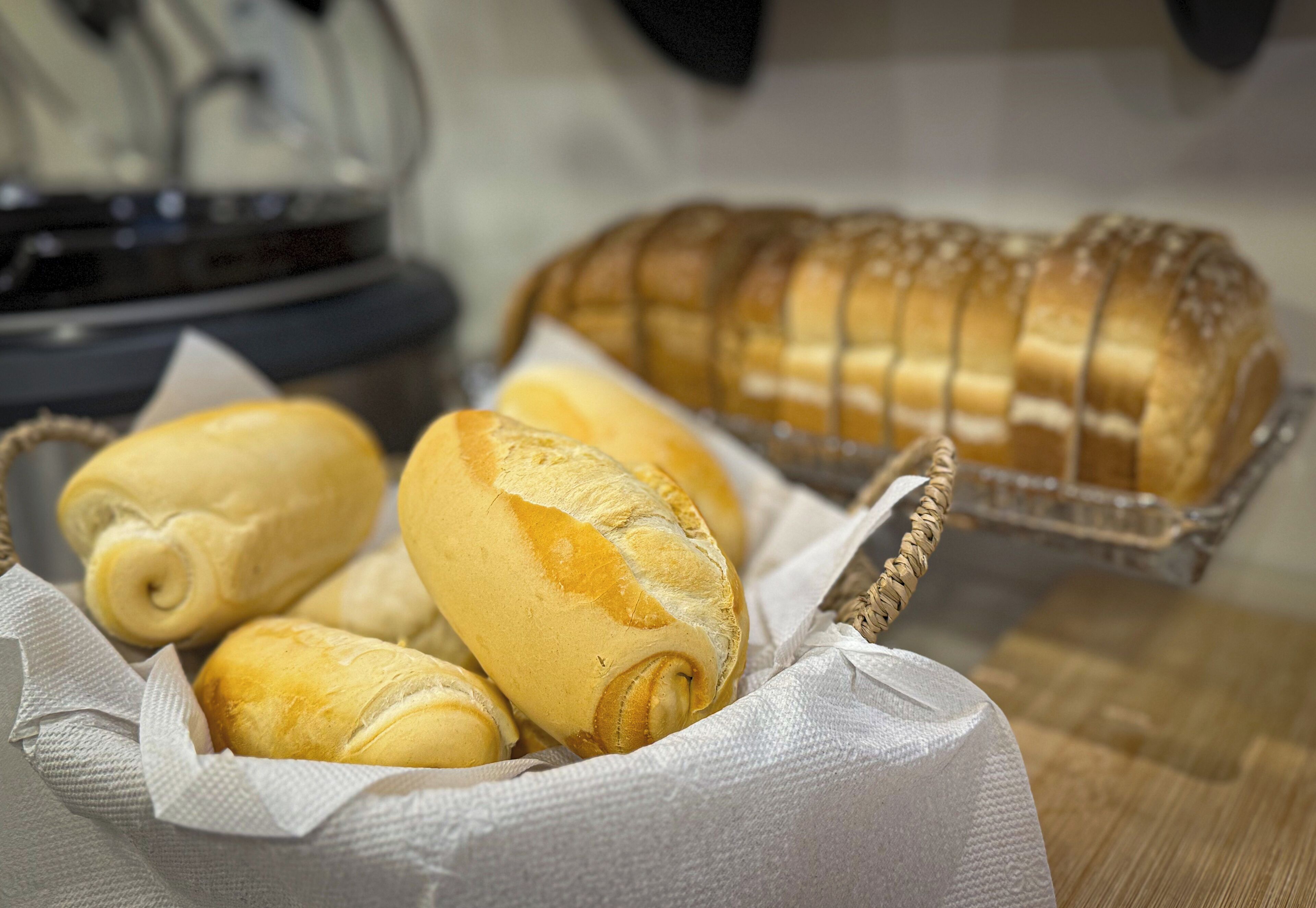 A basket of freshly baked bread rolls and a loaf of sliced bread on a kitchen counter.