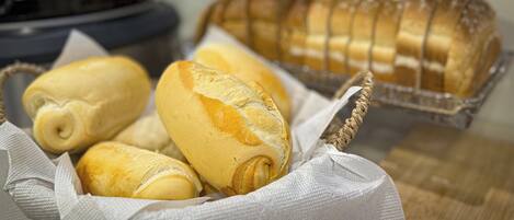 A basket of freshly baked bread rolls and a loaf of sliced bread on a kitchen counter.