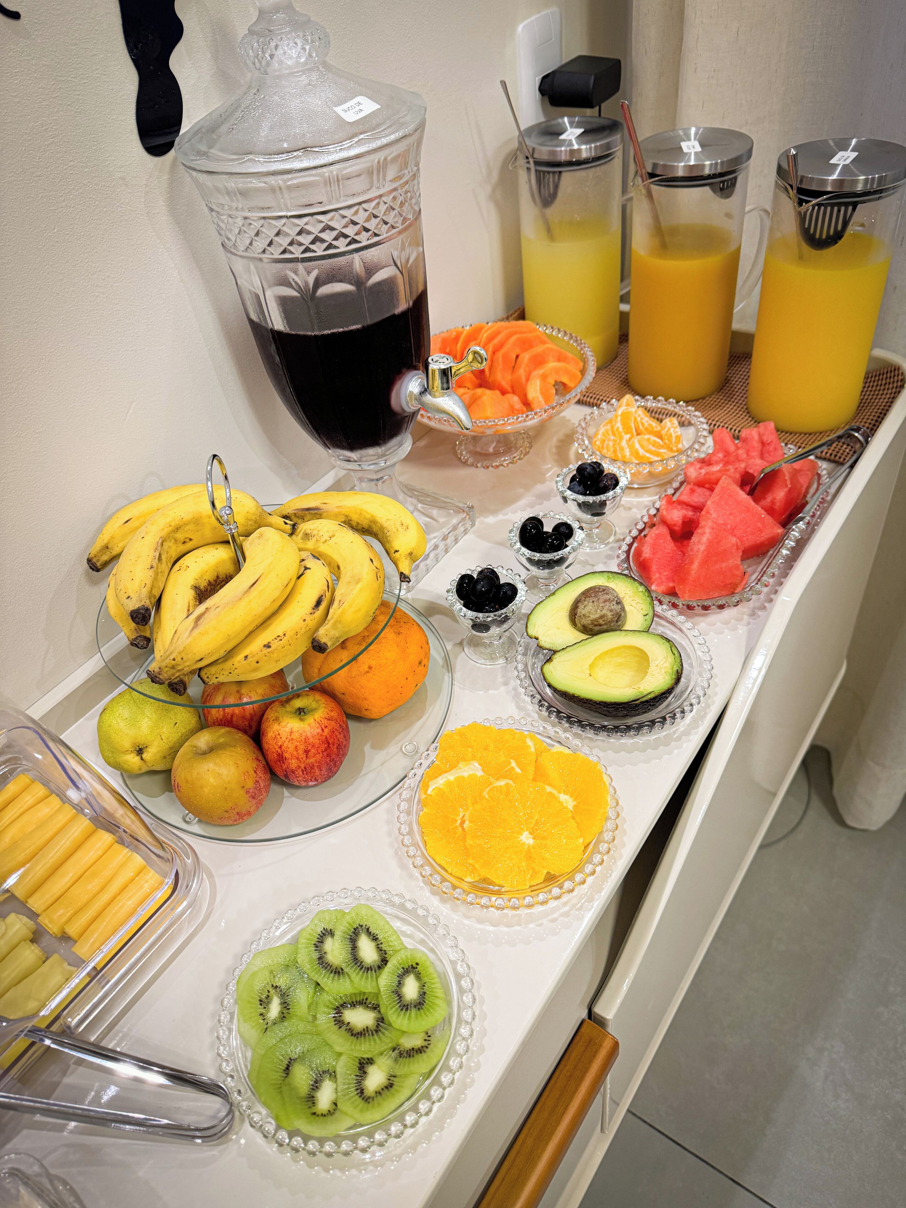 Un bufé de desayuno con diversas frutas, un dispensador de jugo y una cafetera.