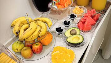 Un bufé de desayuno con diversas frutas, un dispensador de jugo y una cafetera.