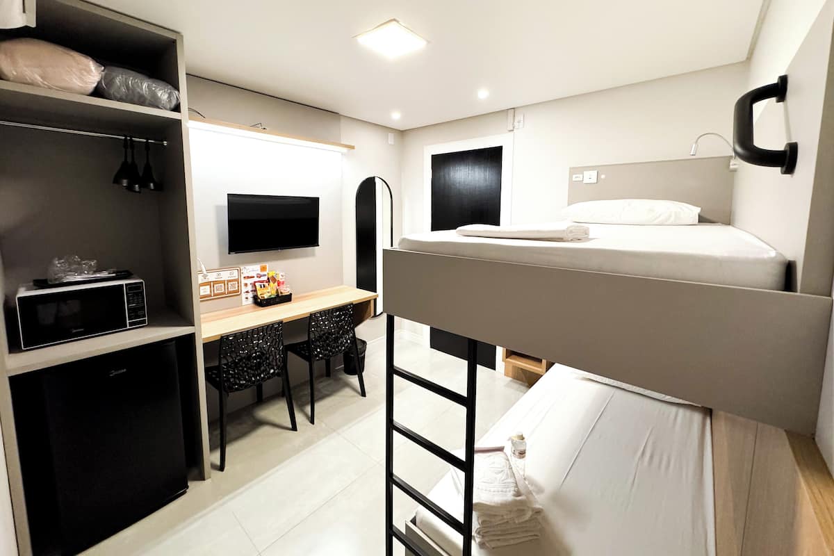 A compact hotel room with bunk beds, a desk with a chair, a microwave, a TV, and a wardrobe.