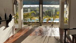 Amplia habitación con un gran ventanal con vistas a una piscina y zonas verdes.
