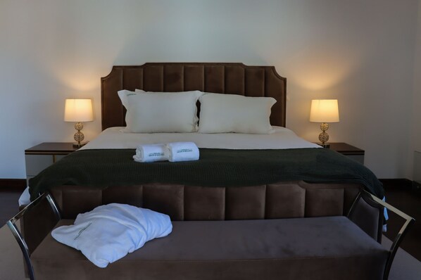 A neatly made bed with a brown headboard, two pillows, and a green blanket. There are two bedside lamps on either side of the bed. A white towel and a rolled-up towel are placed on the bed. - Santar m Private Pool Sauna Gym Villa (Santarém)