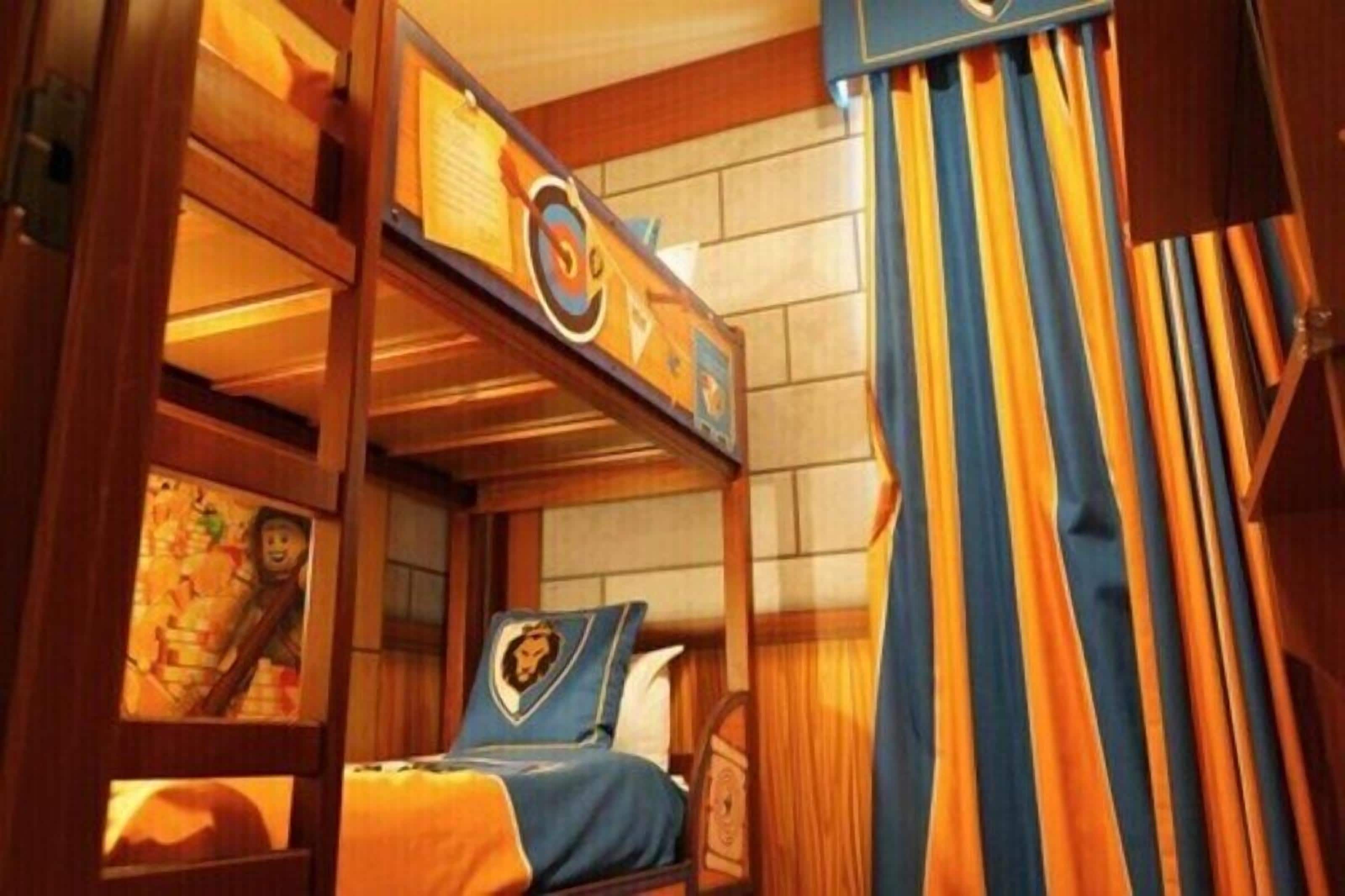 A bunk bed room with a wooden ladder, a bed with a lion emblem, and striped curtains.