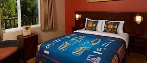 A hotel room with a large bed, a window with curtains, a wall mural, and a nightstand with a lamp.