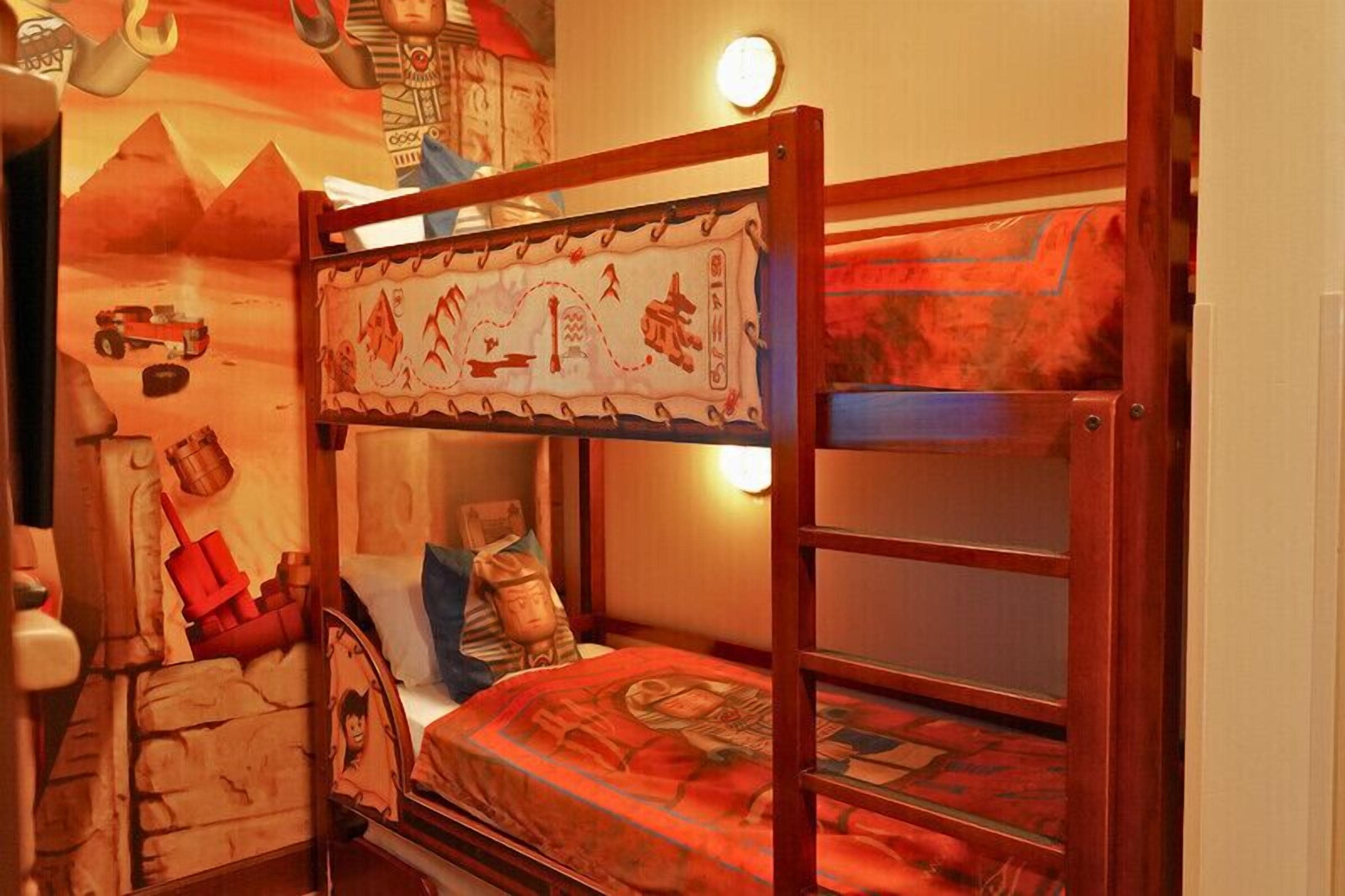 Lliri amb literes decorat amb un mural temàtic del desert, una tauleta de nit i una làmpada penjada a la paret.