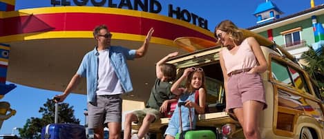 A family at the entrance of the LEGO Land Hotel, with a vintage car and luggage.