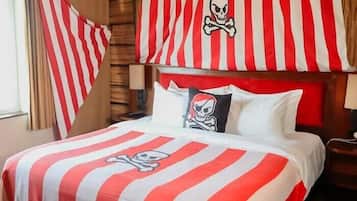 Una habitación con una cama decorada con ropa de cama a rayas rojas y blancas, una almohada con calavera y tibias cruzadas, y una cortina a rayas.