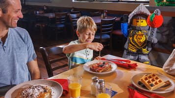 A dining table with plates of food, a glass of juice, and a waffle.