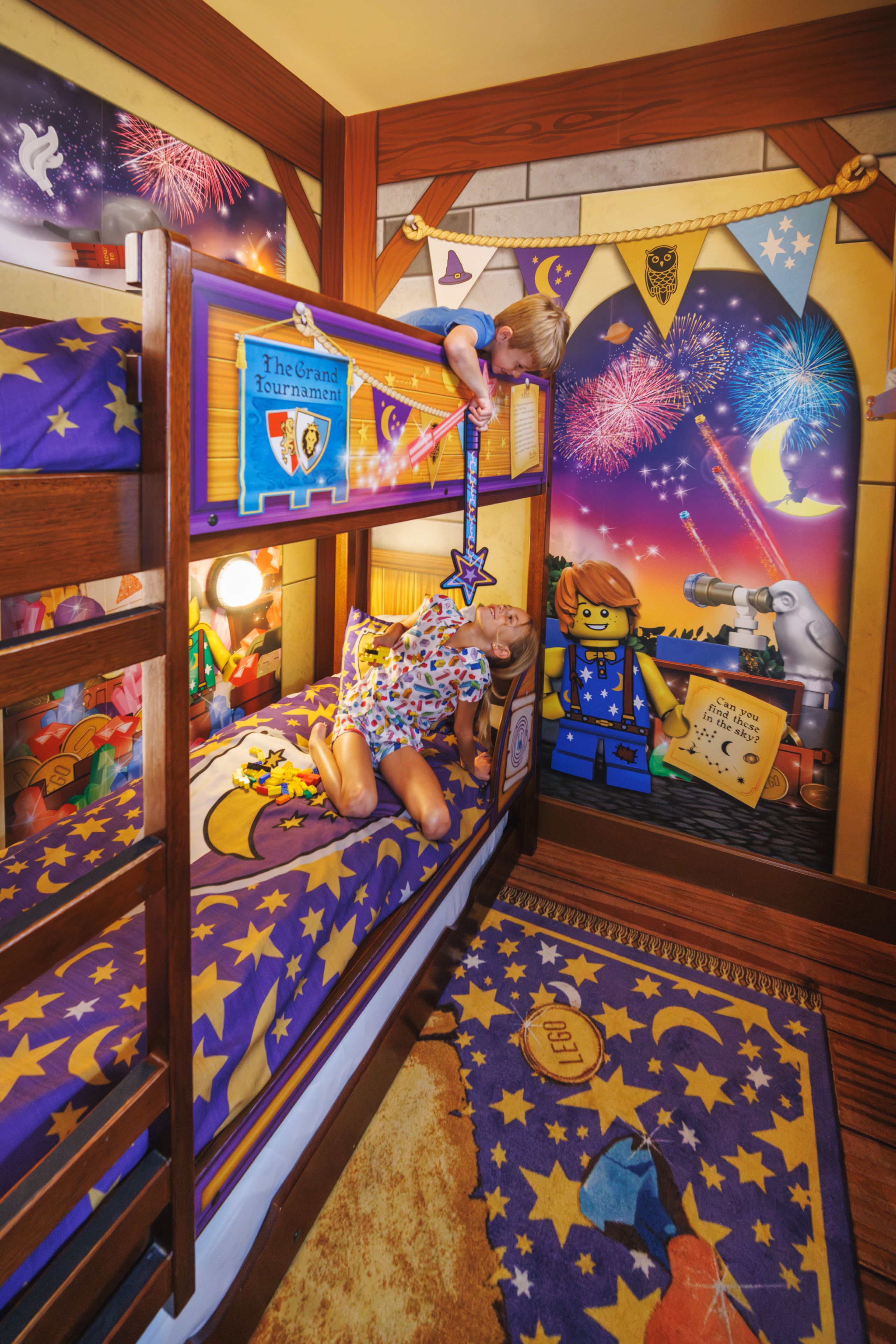 Un lit superposé pour enfants décoré sur le thème d’une nuit étoilée, comprenant un télescope et un livre intitulé « Le Grand Tournoi ».