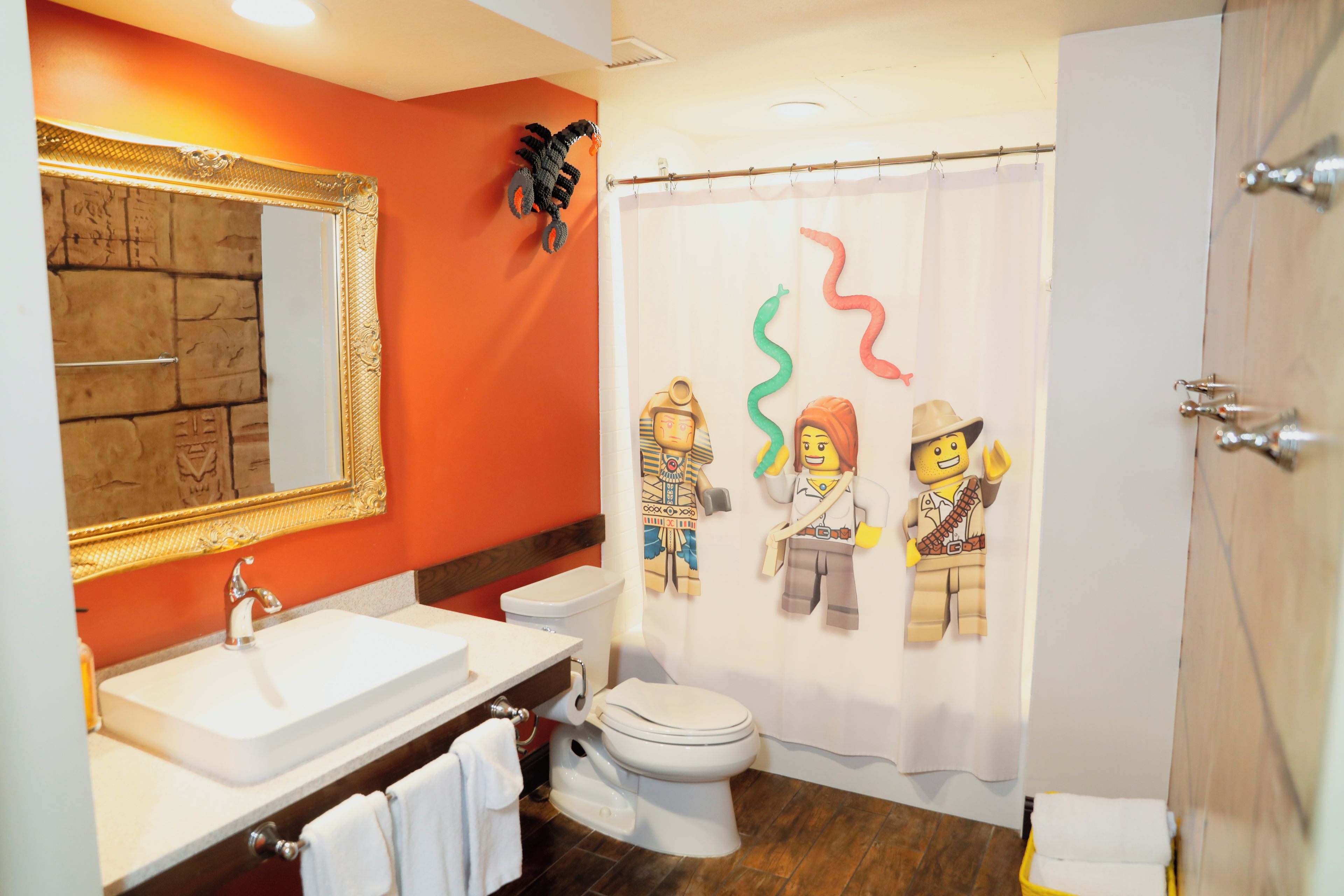 Een badkamer met een wit wastafel, een toilet en een douchegordijn met een LEGO-figuur ontwerp.