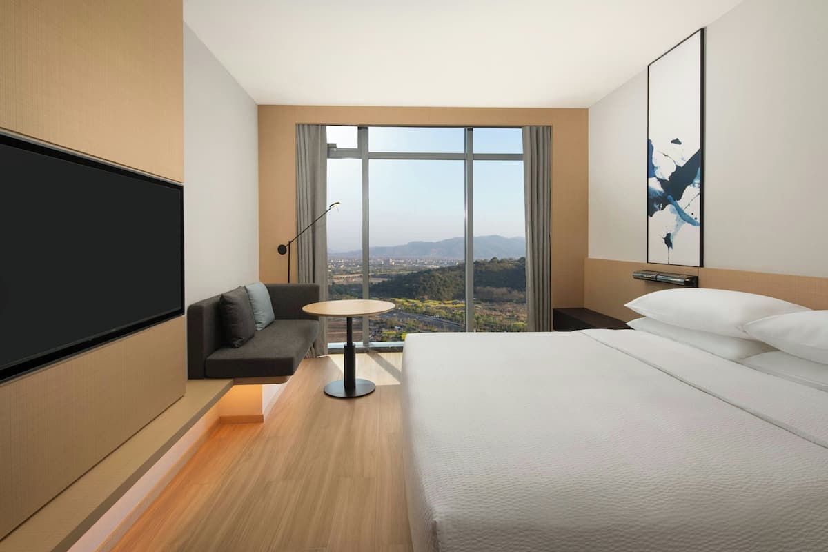 A modern hotel room with a large bed, a sofa, a small table, and a TV.