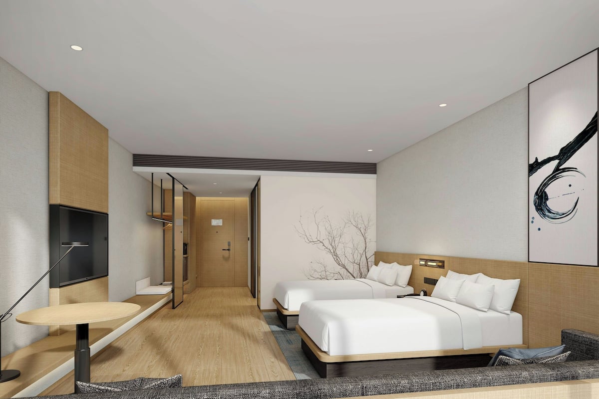 A modern hotel room with two beds, a flat-screen TV, a small table, and a large abstract painting on the wall.