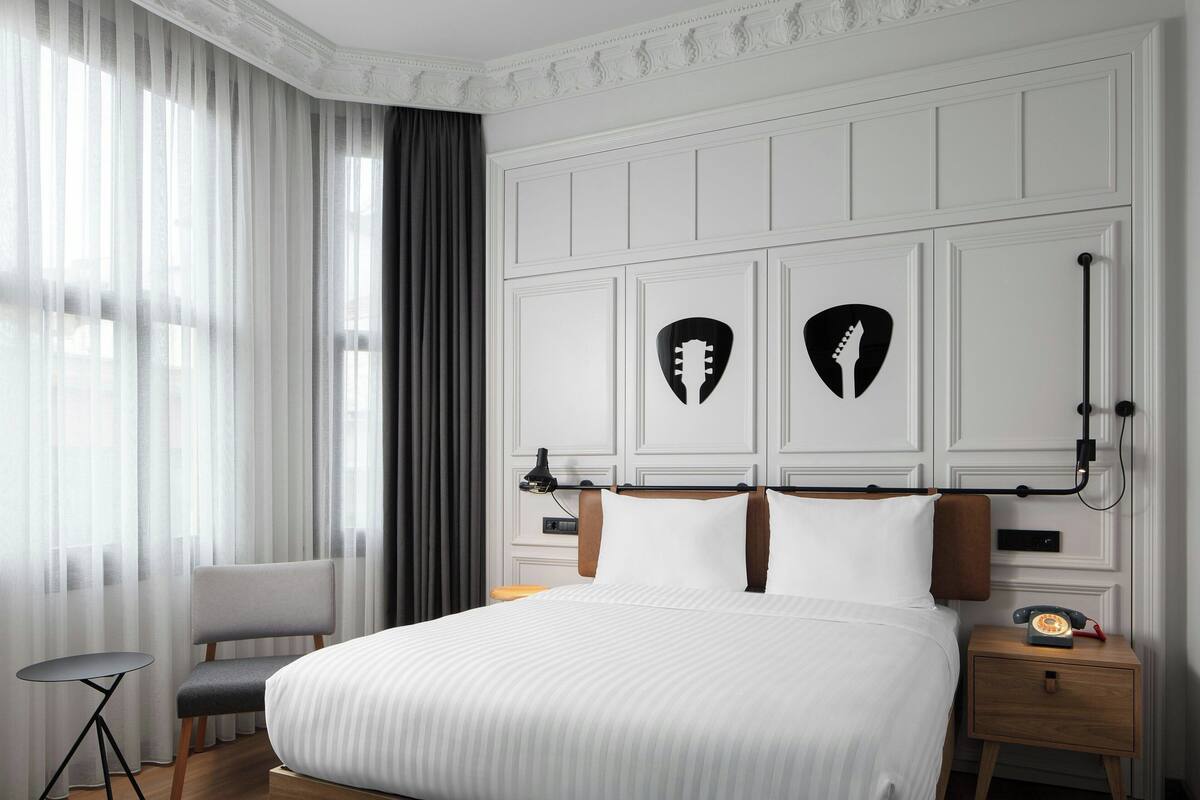 A hotel room with a large bed, a chair, a nightstand with a telephone, and a wall-mounted lamp.