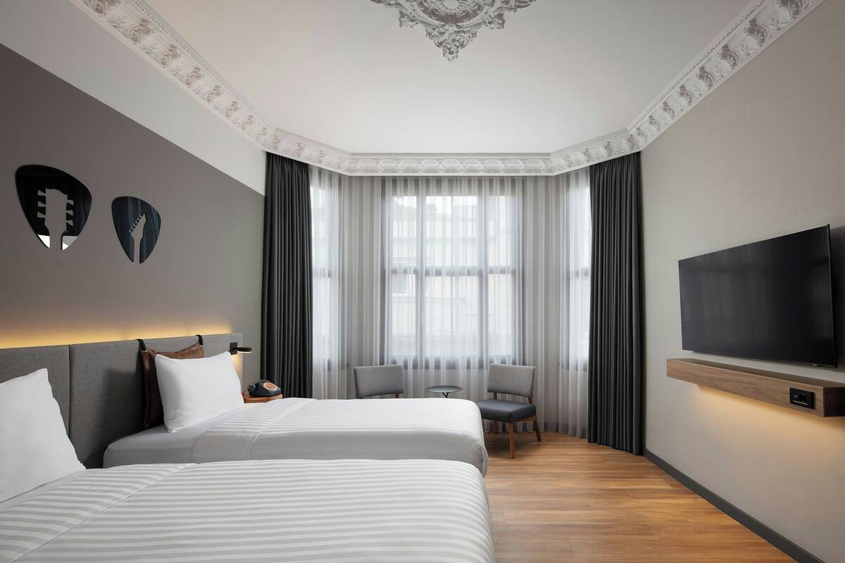 A modern hotel room with two beds, a TV, a small table, and a chair.