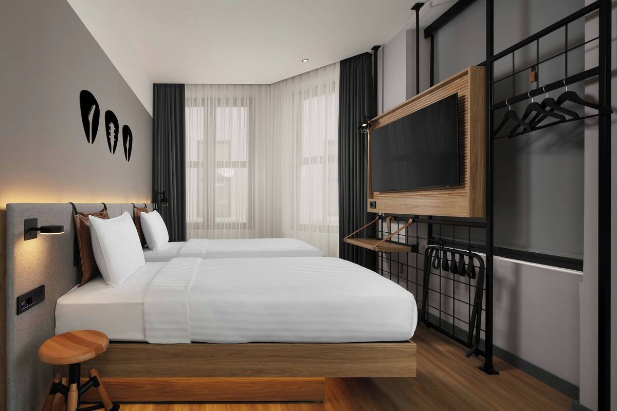 A modern hotel room with a large bed, a TV mounted on a wooden panel, and a coat rack.