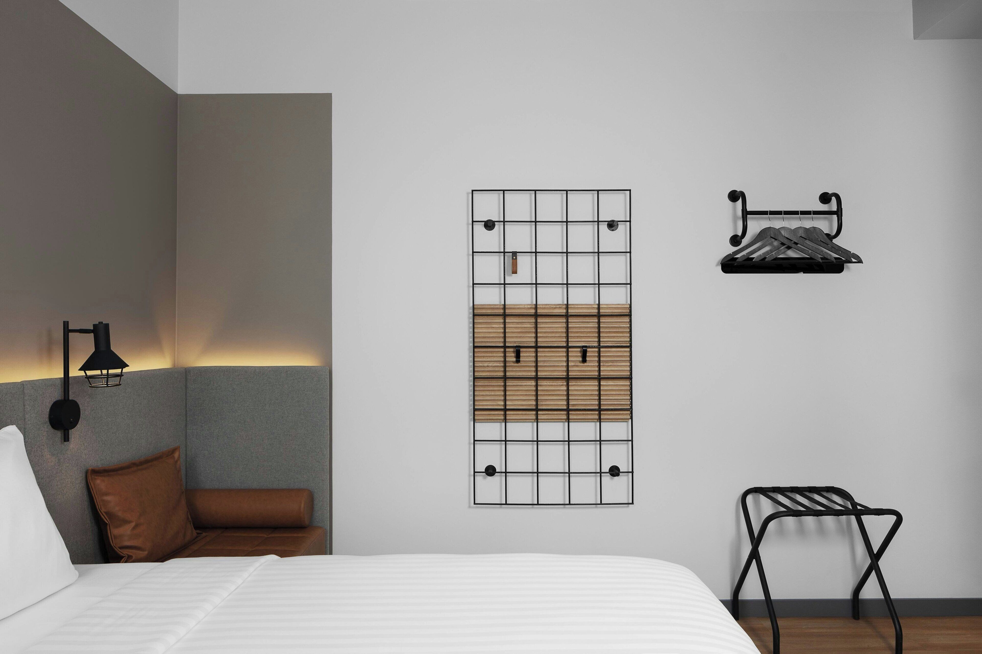 Une chambre d’hôtel moderne équipée d’un lit, d’un porte-serviettes fixé au mur, d’un petit tabouret et d’une œuvre d’art murale.