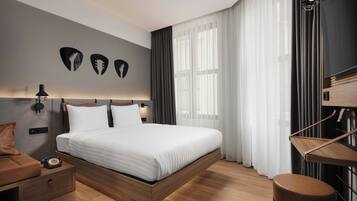 Una habitación de hotel moderna con una cama de madera, una mesita de noche, un escritorio y un gran ventanal con cortinas.