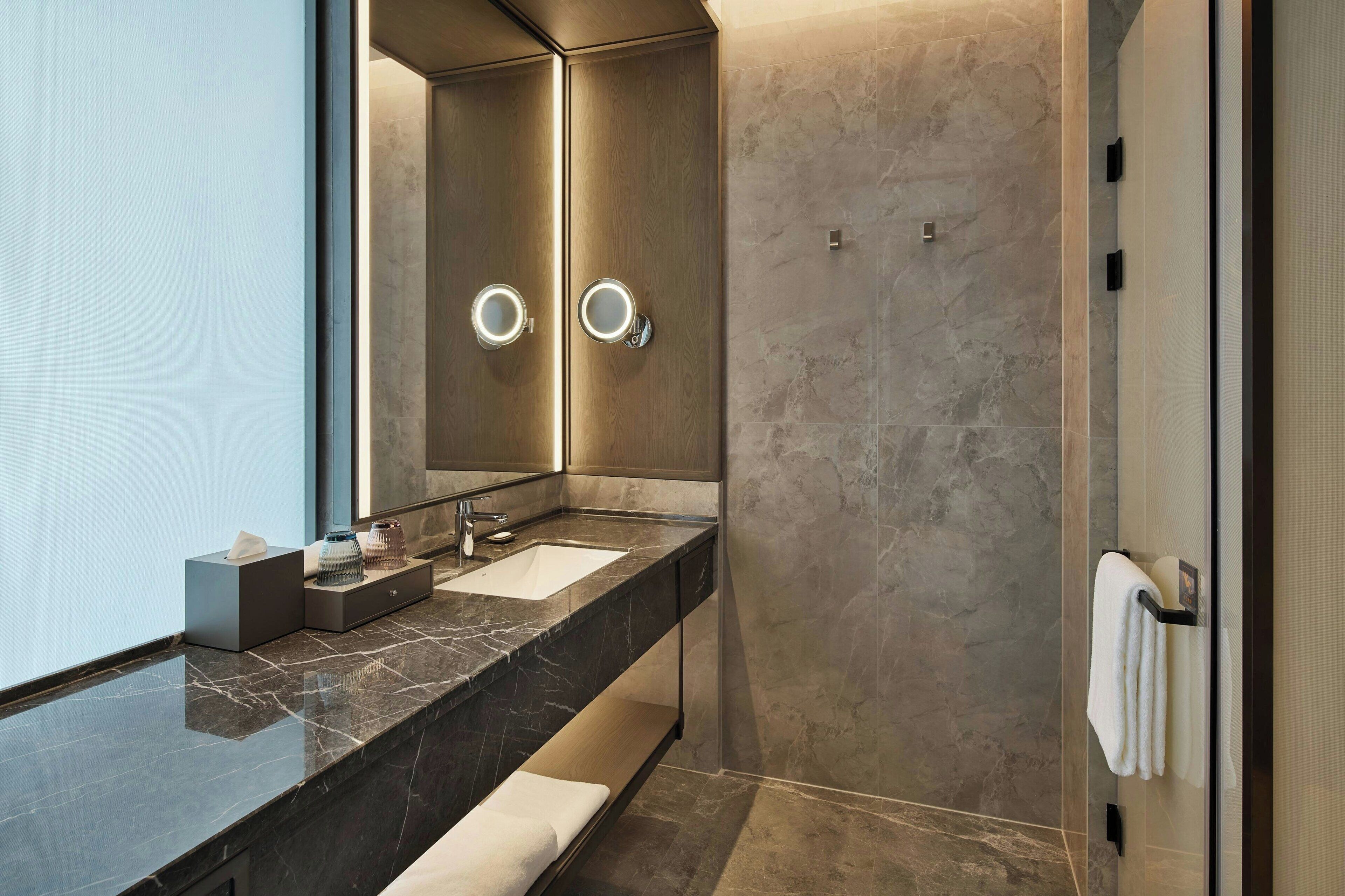 A modern bathroom with a marble countertop, a large mirror, and a towel rack.