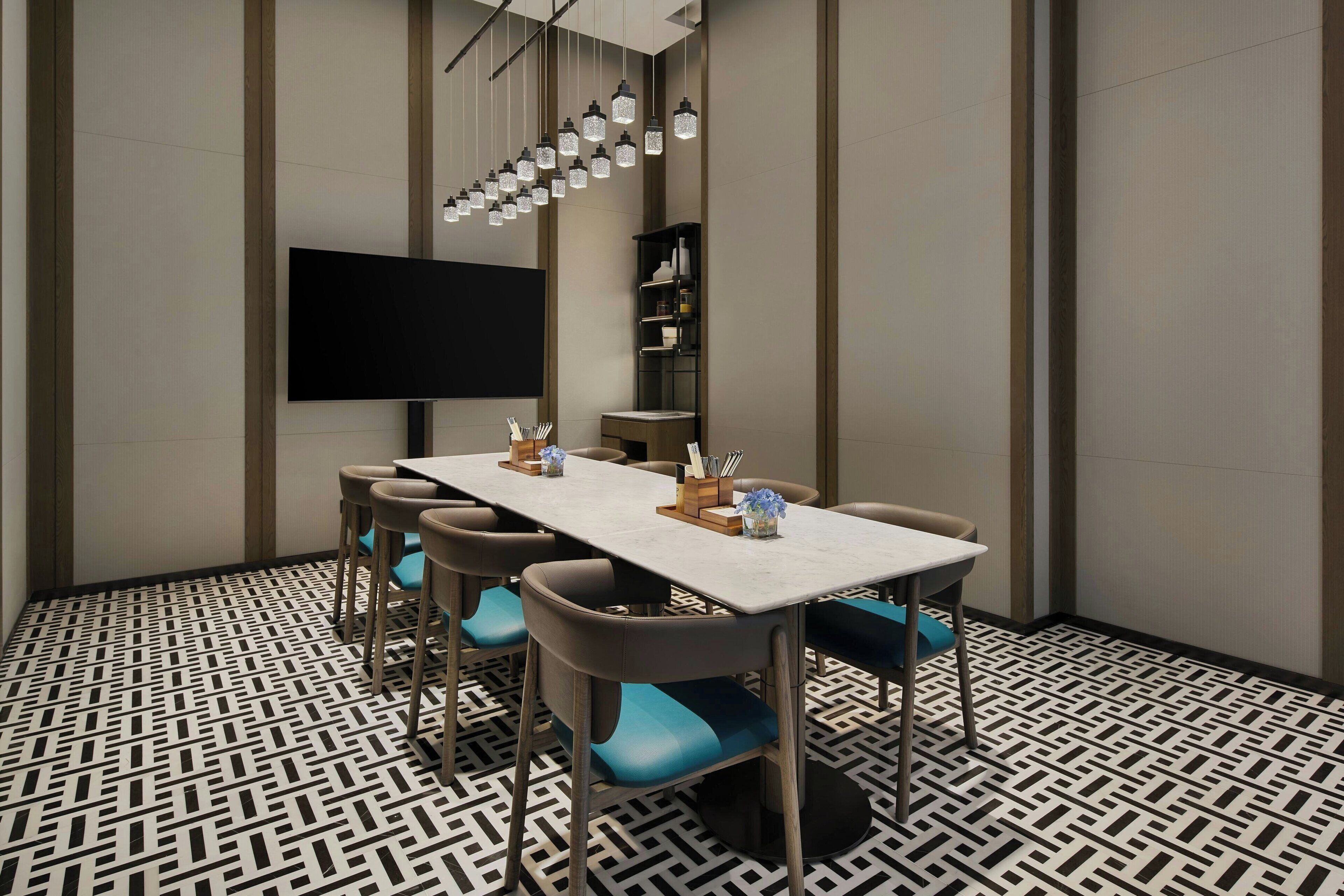 A conference room with a long table, chairs, a flat-screen TV, and a patterned floor.