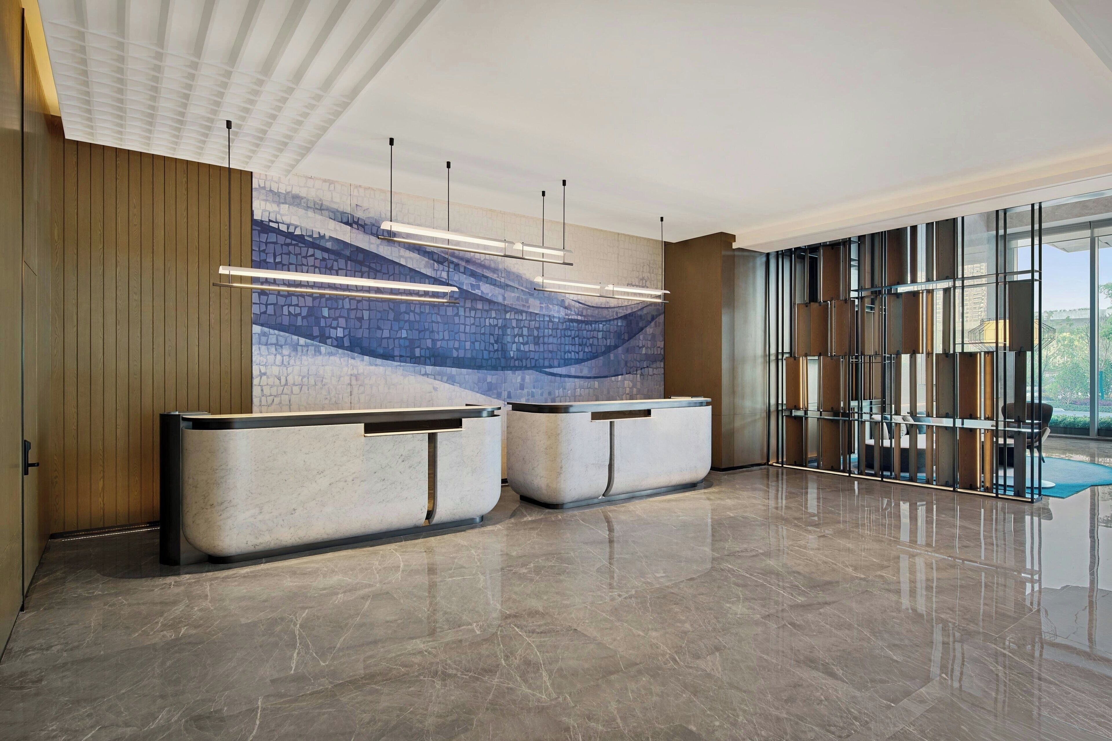 Un área de recepción moderna con suelo de mármol, dos mostradores de recepción, un amplio mural abstracto y un panel de vidrio con vistas.