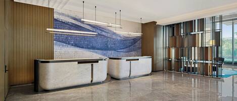 Un área de recepción moderna con suelo de mármol, dos mostradores de recepción, un amplio mural abstracto y un panel de vidrio con vistas.