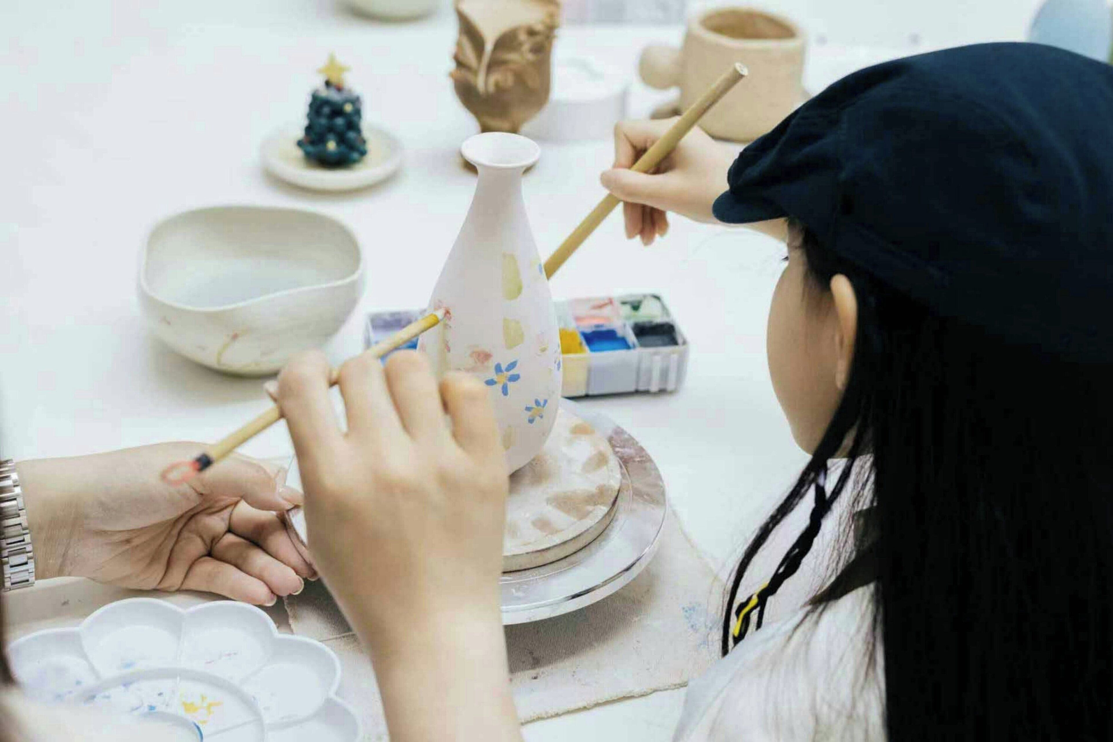 A person painting a ceramic vase with a floral pattern.