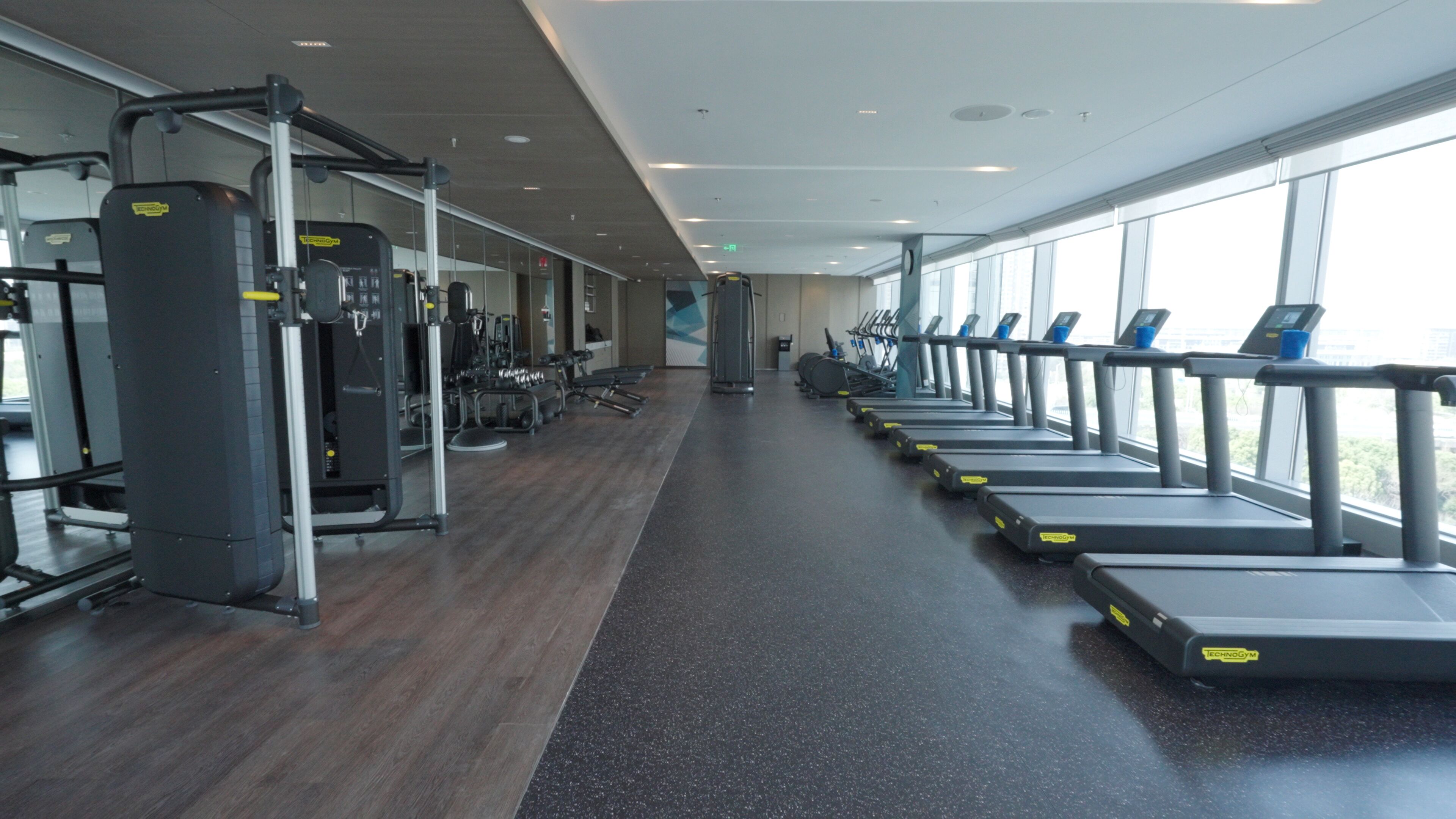 A gym with treadmills, weight machines, and a wooden floor.