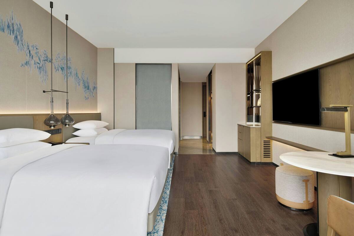 Une chambre d’hôtel moderne dotée d’un grand lit, d’un téléviseur à écran plat, d’une table de chevet et d’une lampe fixée au mur.