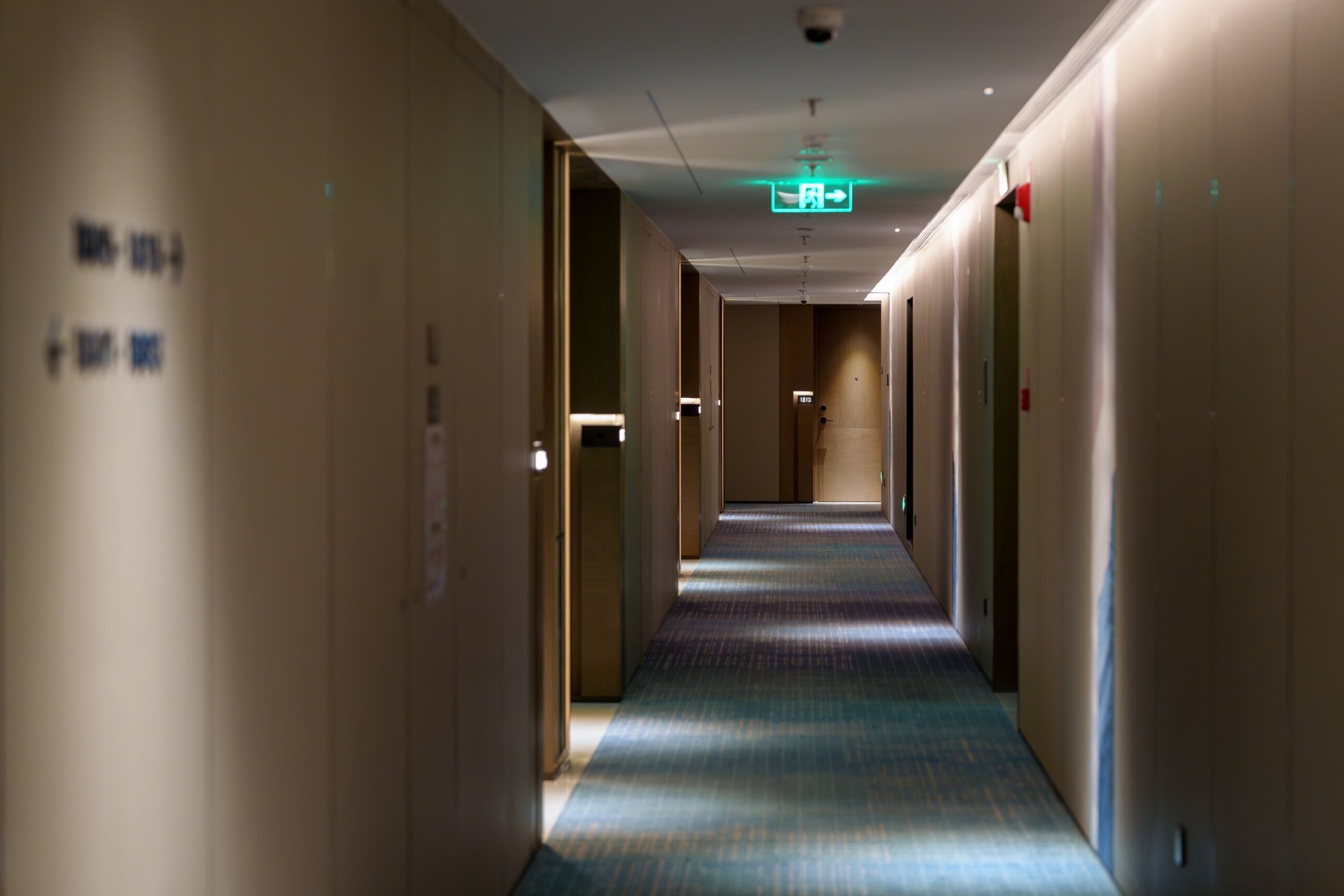 Corridoio di un albergo con porte su entrambi i lati, una moquette decorata e un segnale di uscita al soffitto.