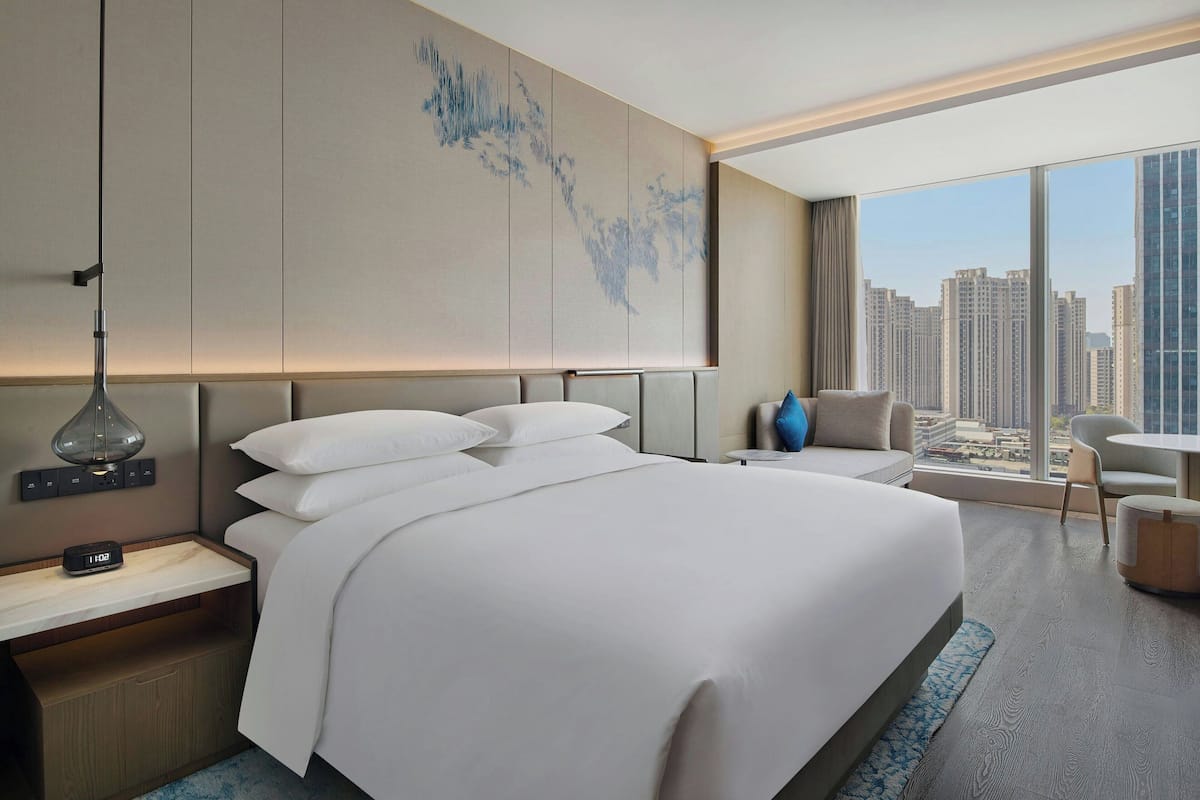Une chambre d’hôtel moderne, dotée d’un grand lit, d’une table de chevet, d’un bureau, d’une chaise et offrant une vue sur le paysage urbain.
