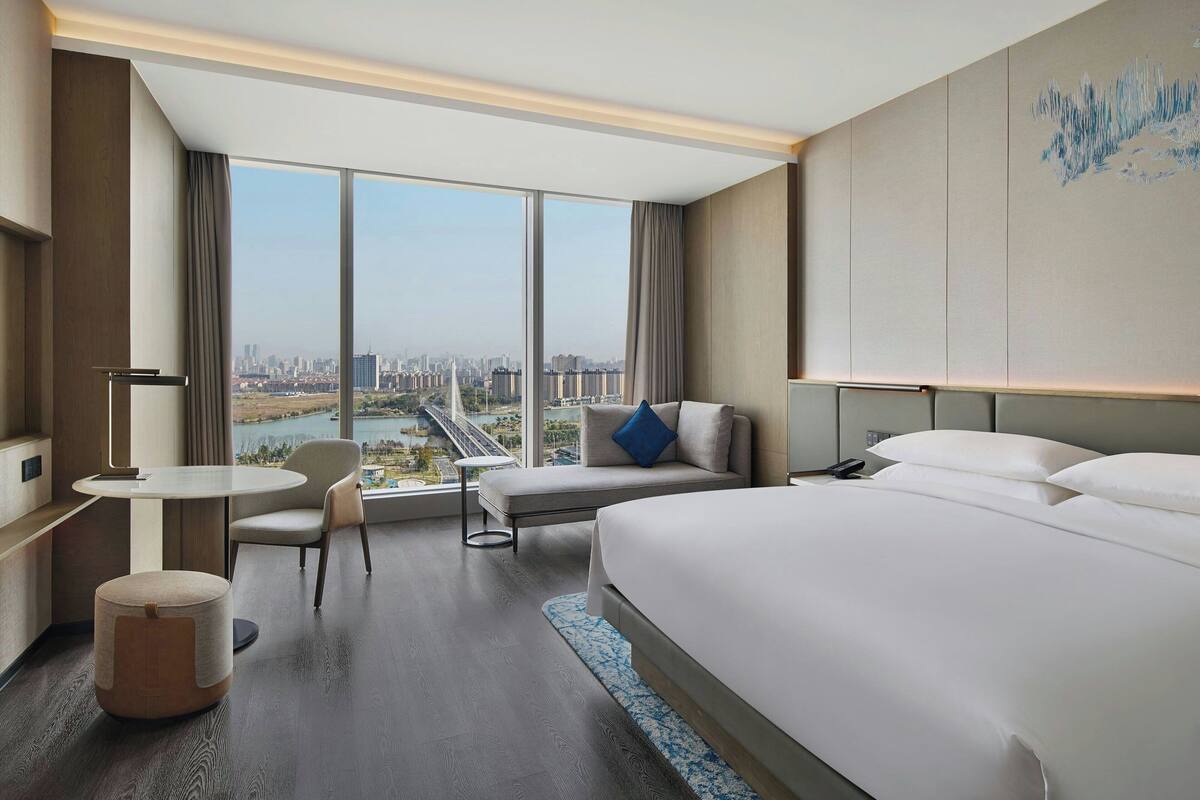 Une chambre d’hôtel moderne avec un grand lit, un coin salon offrant une vue sur la ville et une petite table.