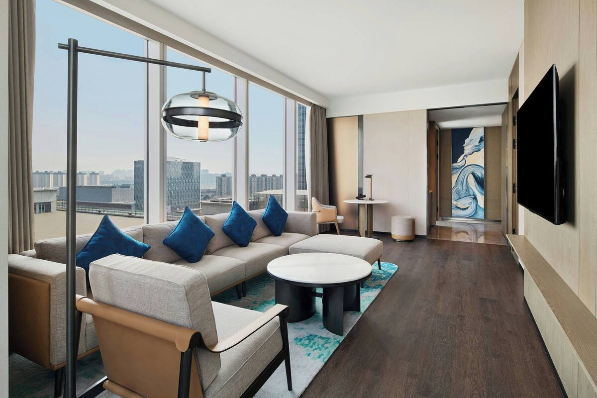 Une chambre d’hôtel moderne, dotée d’un grand canapé, d’une table basse ronde et d’un téléviseur à écran plat fixé au mur.