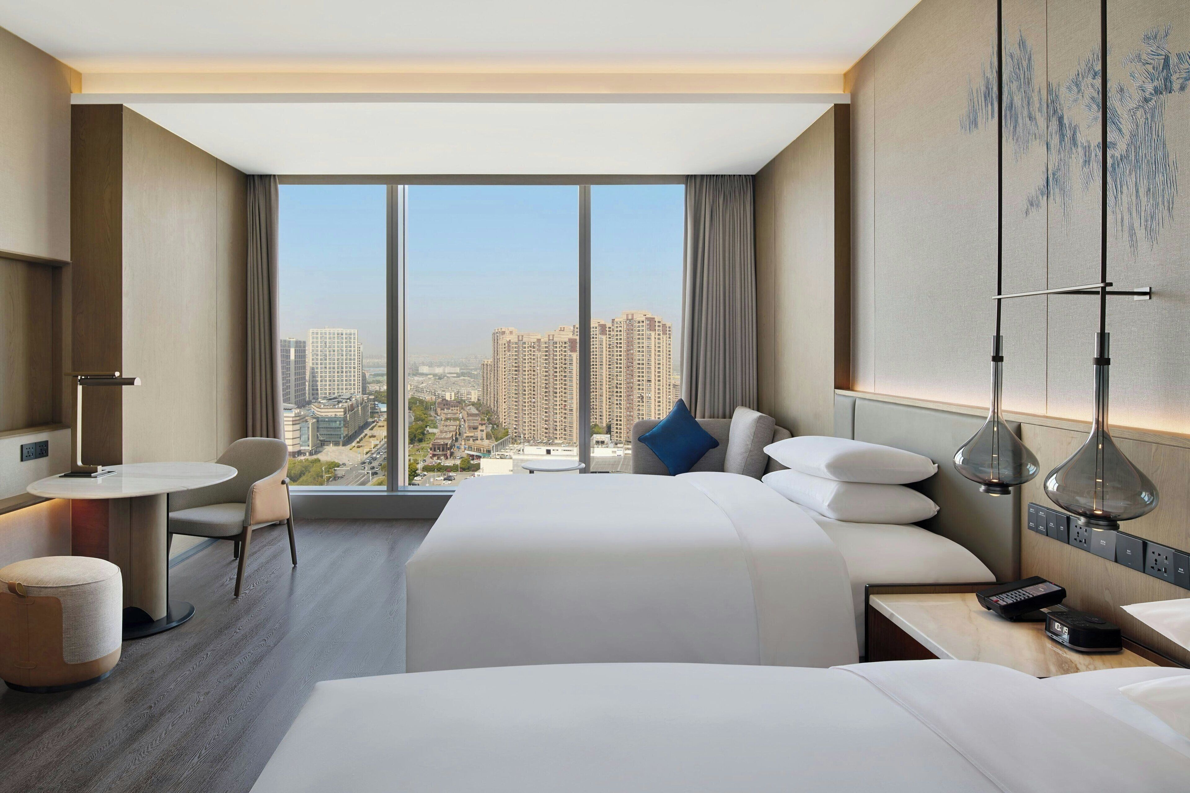A hotel room with a large window, a bed, a desk, and a chair.