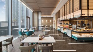 A modern restaurant with a long counter, seating area with tables and chairs, and large windows offering a view of the city. - Courtyard By Marriott Nantong (Nantong)