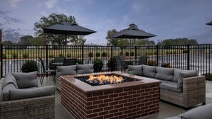 An outdoor patio area with a brick fire pit, grey cushioned seating, and two umbrellas. - Fairfield By Marriott Inn & Suites Weldon (Weldon)