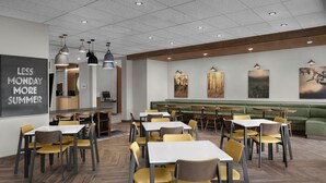 A modern restaurant with wooden flooring, yellow and grey chairs, and tables. There are ceiling lights and artwork on the walls. - Fairfield By Marriott Inn & Suites Weldon (Weldon)