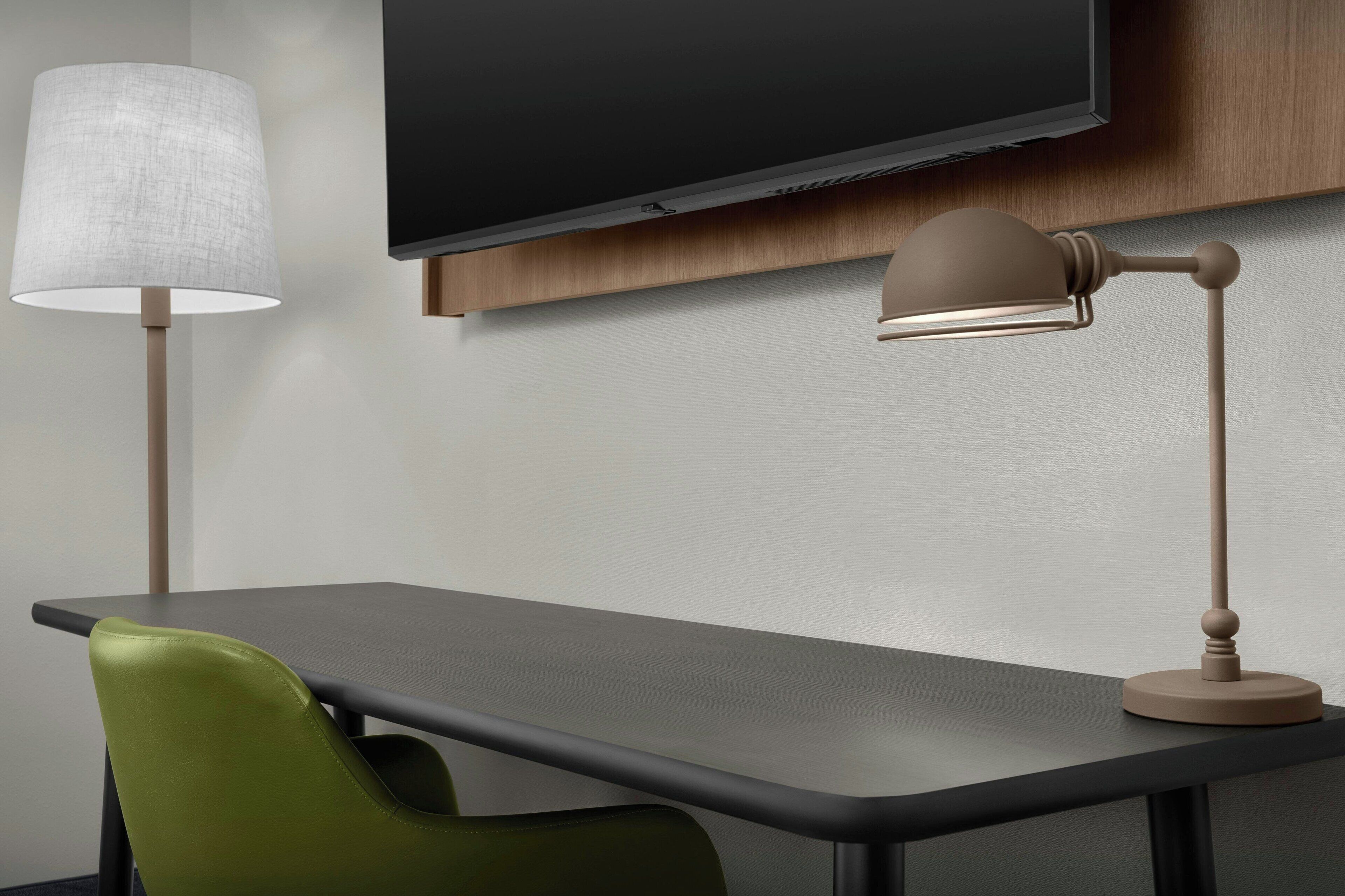Un escritorio moderno con una televisión de pantalla plana montada encima, una lámpara y una silla verde.