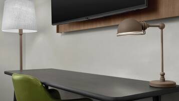 Un escritorio moderno con una televisión de pantalla plana montada encima, una lámpara y una silla verde.