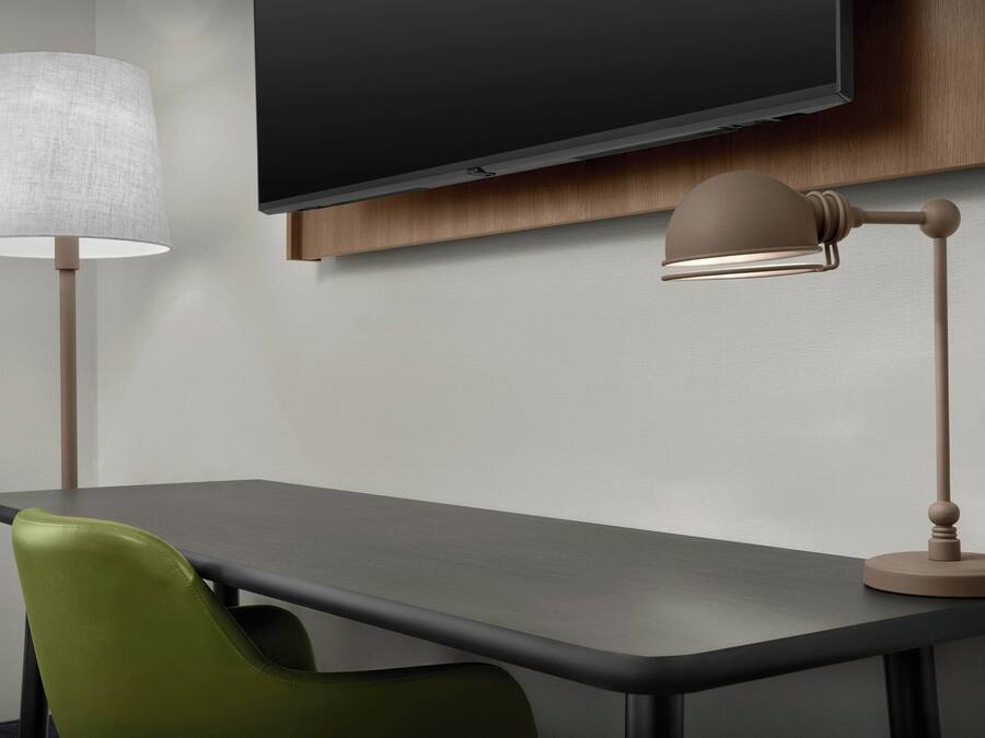 Un escritorio moderno con una televisión de pantalla plana montada encima, una lámpara y una silla verde.