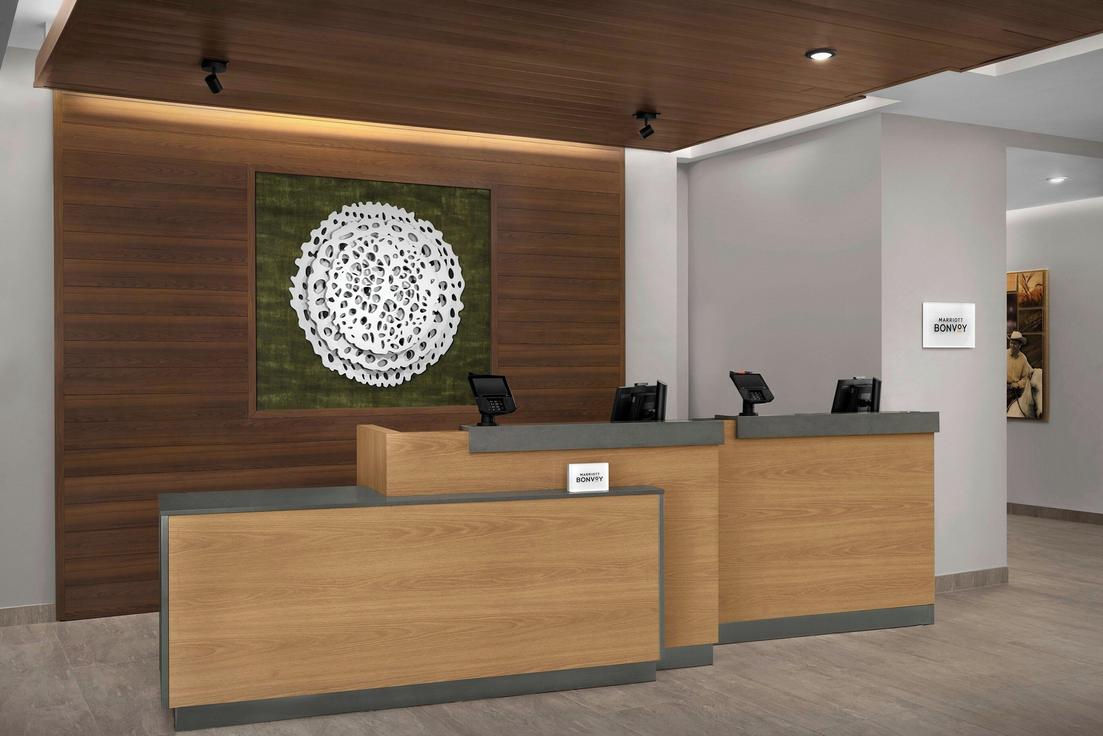 A hotel reception desk with a wooden finish, a nameplate, and a large abstract artwork on the wall.