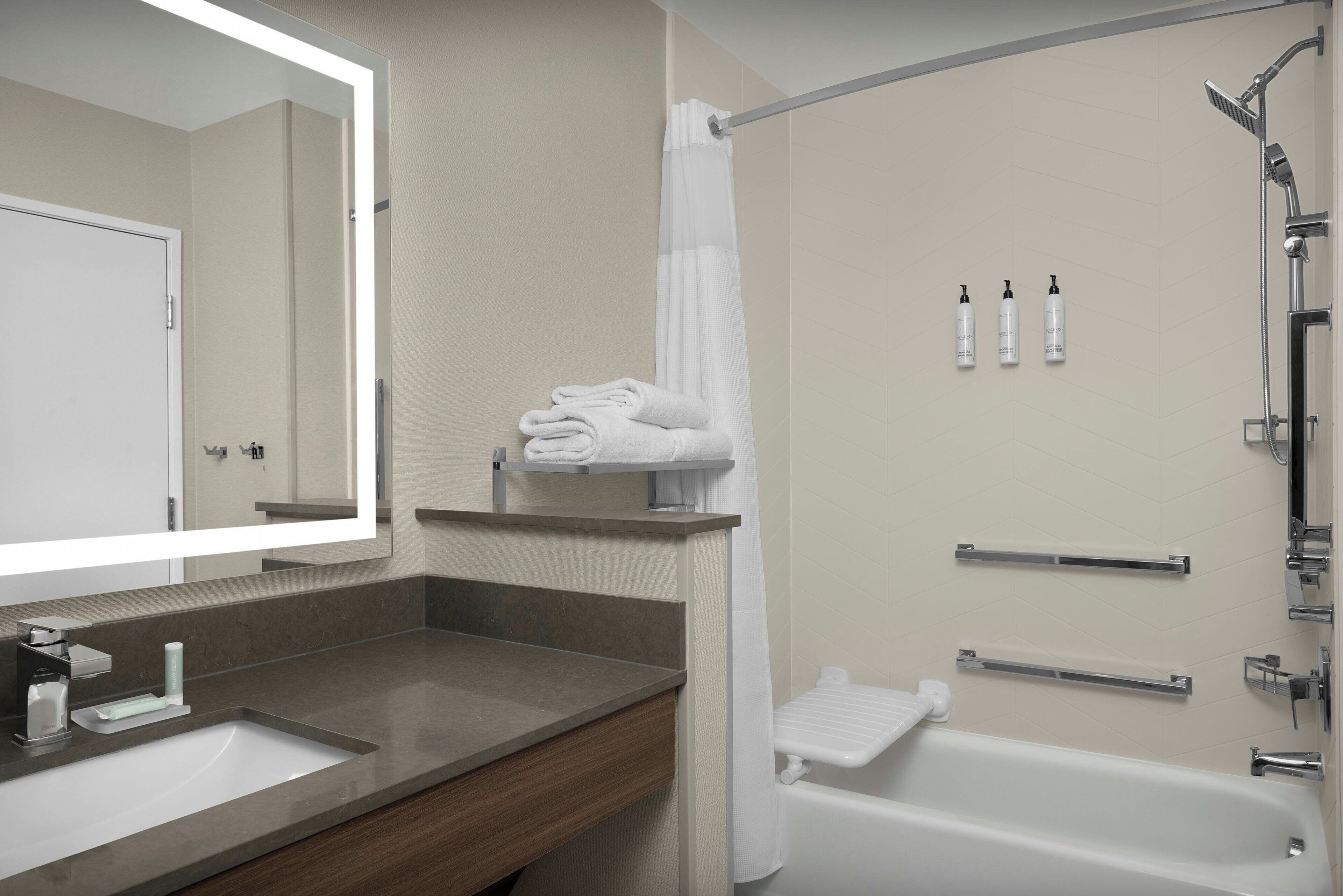 A modern bathroom with a sink, mirror, towel rack, shower, and toiletries.