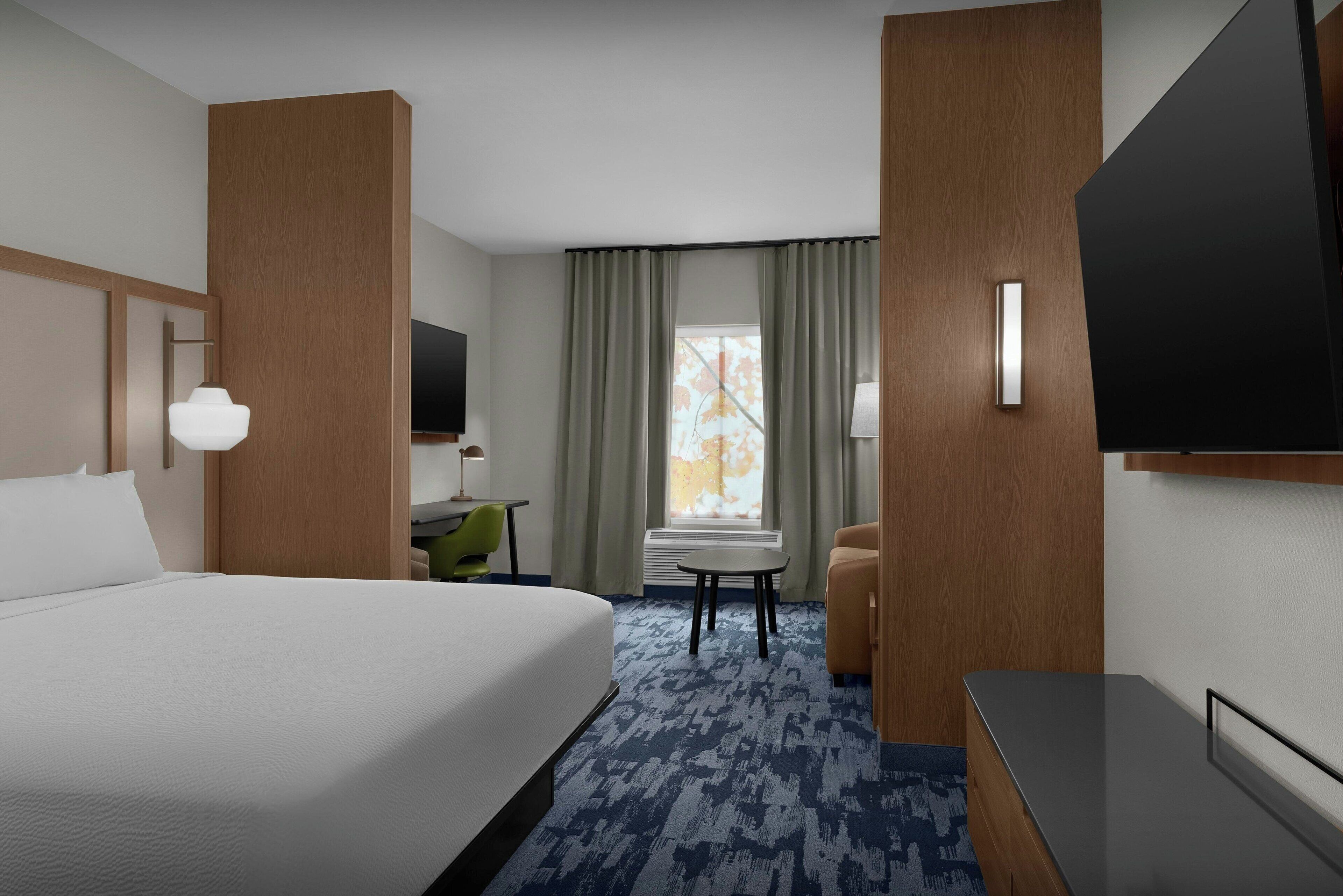 A hotel room with a large bed, a desk, a chair, a TV, and a window with curtains.